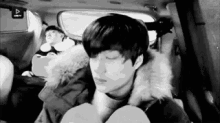 a black and white photo of a boy sitting in the back seat of a car .