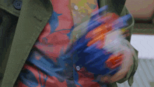 a person wearing a green trench coat and a colorful shirt is holding a colorful object