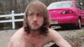 a shirtless man sitting in front of a pink car with a new jersey license plate that says jugg1es
