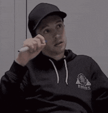 a man wearing a hat and a black hoodie is talking on a cell phone .