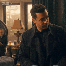 a man in a black trench coat is standing in front of a window with saint pierre written on the bottom