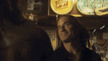 a man with long hair is smiling in front of a sign that says ' beer ' on it .