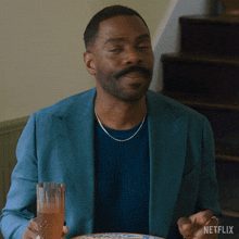 a man in a blue jacket is holding a glass with netflix written on the bottom right