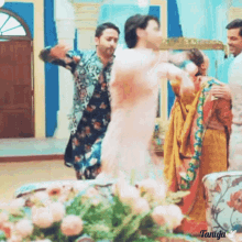 a group of people are dancing in a room with flowers in the foreground and the name tanuja at the bottom
