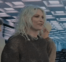 a woman with blonde hair is wearing a sweater and a necklace while standing in a room .