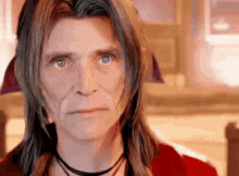 a man with long hair and a choker around his neck is making a funny face .