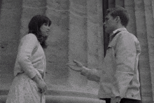 a man and a woman are standing next to each other and talking in front of a building .