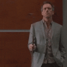 a man in a suit and tie is standing in front of a wooden wall holding a cell phone .
