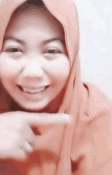 a woman wearing a pink hijab is smiling and pointing at the camera