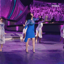 a woman in a blue dress is dancing on a stage in front of a choir with the word max on the bottom