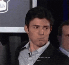 a man in a suit and striped shirt talks into a microphone in front of a sign that says ian