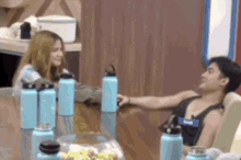 a man and woman are sitting at a table with water bottles .