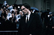 a man in a suit and tie stands in front of a crowd of people taking pictures