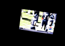 a tv screen shows a group of people standing on a field with the number 22 on the bottom right