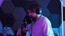 a man wearing headphones stands in front of a microphone with gifrun.com written on the bottom right