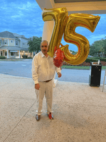 a man holds a red balloon in front of a large number 75 balloon