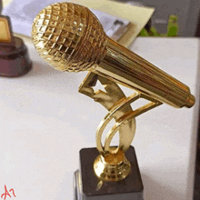 a gold microphone trophy with the letter a written on the bottom