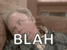a man is laying on a couch and making a funny face with the word blah on his face .