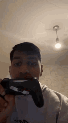 a man holding a video game controller with a light bulb hanging from the ceiling behind him