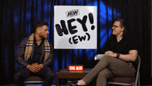 two men sitting in front of a sign that says hey ( ew )