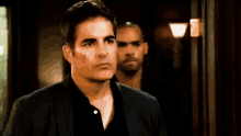a man in a black suit is standing next to another man in a black shirt .