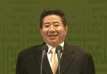 a man in a suit and tie stands in front of two microphones with korean writing on the bottom