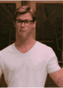 a man wearing glasses and a white t-shirt is standing in front of a door .