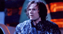 a man with long hair is wearing a sequined jacket and looking at the camera .