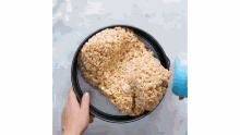 a person is holding a pan filled with rice krispie treats on a table .