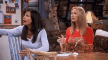 two women sit at a table in front of a refrigerator that has a picture of the friends on it