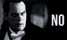 a man in a tuxedo and bow tie is looking at the camera with the word no behind him .