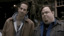 two men are standing next to each other in front of a building and smiling