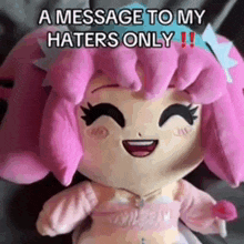 a stuffed doll with pink hair is sitting on a bed and smiling .