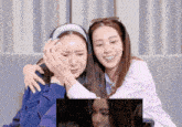 two women are sitting on a couch watching a video and one is crying