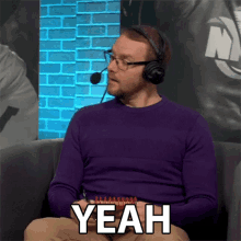 a man wearing headphones and a purple sweater says " yeah "