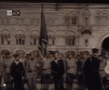 a group of people standing in front of a building with a 24 ack logo on the bottom