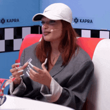 a woman wearing a white nike hat sits in front of a sign that says kappa