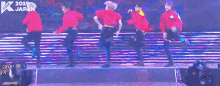 a group of men in red shirts are dancing on a stage in front of a sign that says k pop 2019 japan