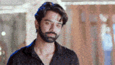 a man with a beard wearing a black shirt is looking at the camera .
