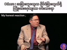 a man in a suit and tie is sitting in front of a black background with the words " my honest reaction " below him