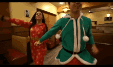 a man and a woman are dancing in a diner . the man is dressed as a santa claus .