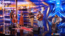 a group of people playing instruments on a stage with a nbc logo