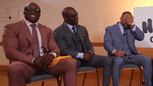 three men in suits are sitting in chairs with one covering his face with his hand