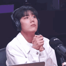 a young man wearing headphones is sitting in front of a microphone with his hands folded .