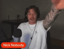 a man wearing headphones stands in front of a microphone with the name nick nobody on the bottom right