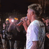 a man drinking from a bottle while standing in front of a crowd of people