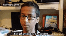a young boy wearing glasses is sitting in front of a computer desk and talking about being arrested for a hoax bomb .