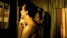a shirtless man wipes his face in front of a mirror
