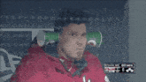 a man sitting in a dugout with cups in his ears and a scoreboard that says pitcher 65 1-0 out