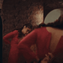a woman in a red dress is looking at her reflection in a mirror